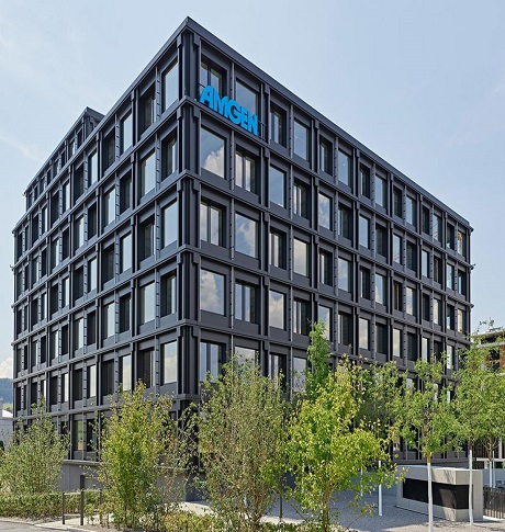 Ein futuristisches Bürogebäude mit schwarzen Fenstern, das Amgen in der Schweiz repräsentiert. Das Holzhochhaus strahlt Eleganz und Innovation aus.